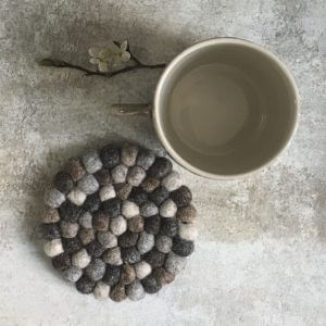 Round felted trivet with a ceramic mug on a textured surface