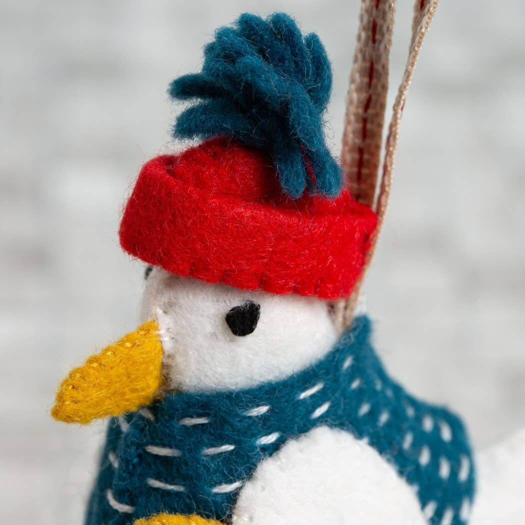 Felted snowman ornament with a red hat and blue scarf against a blurred snowy background
