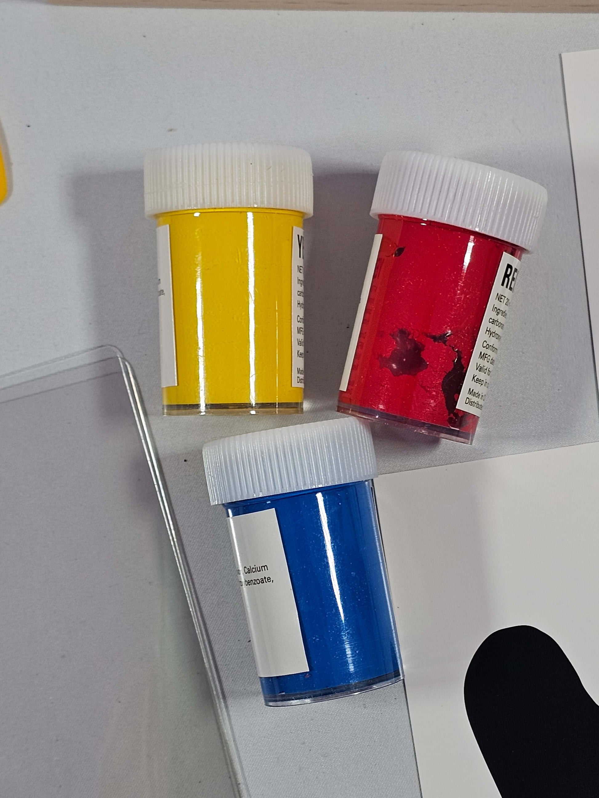 Three jars of acrylic paint in yellow, red, and blue colors for screen printing projects.