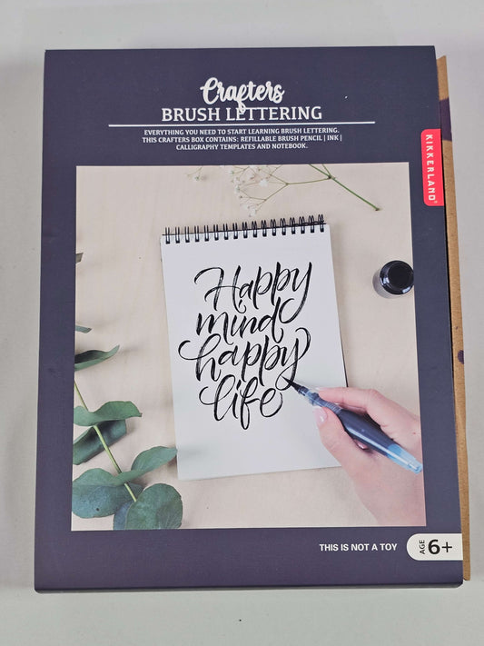 Kikkerland brush lettering kit displaying handwritten notes and tools for modern calligraphy on a crafting table.