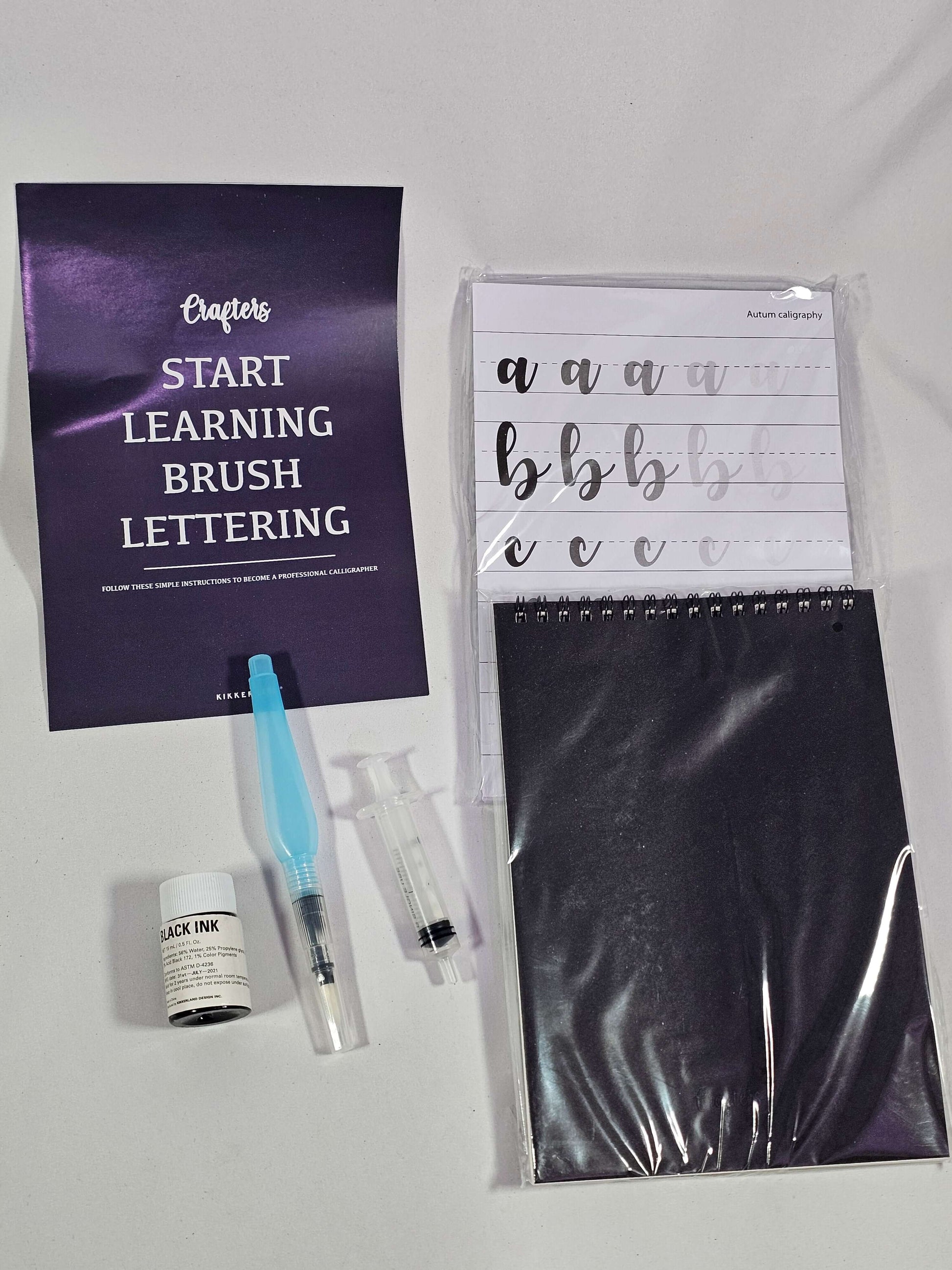 Brush lettering kit contents: instruction sheet, templates, refillable brush, ink, and notebook for modern lettering.