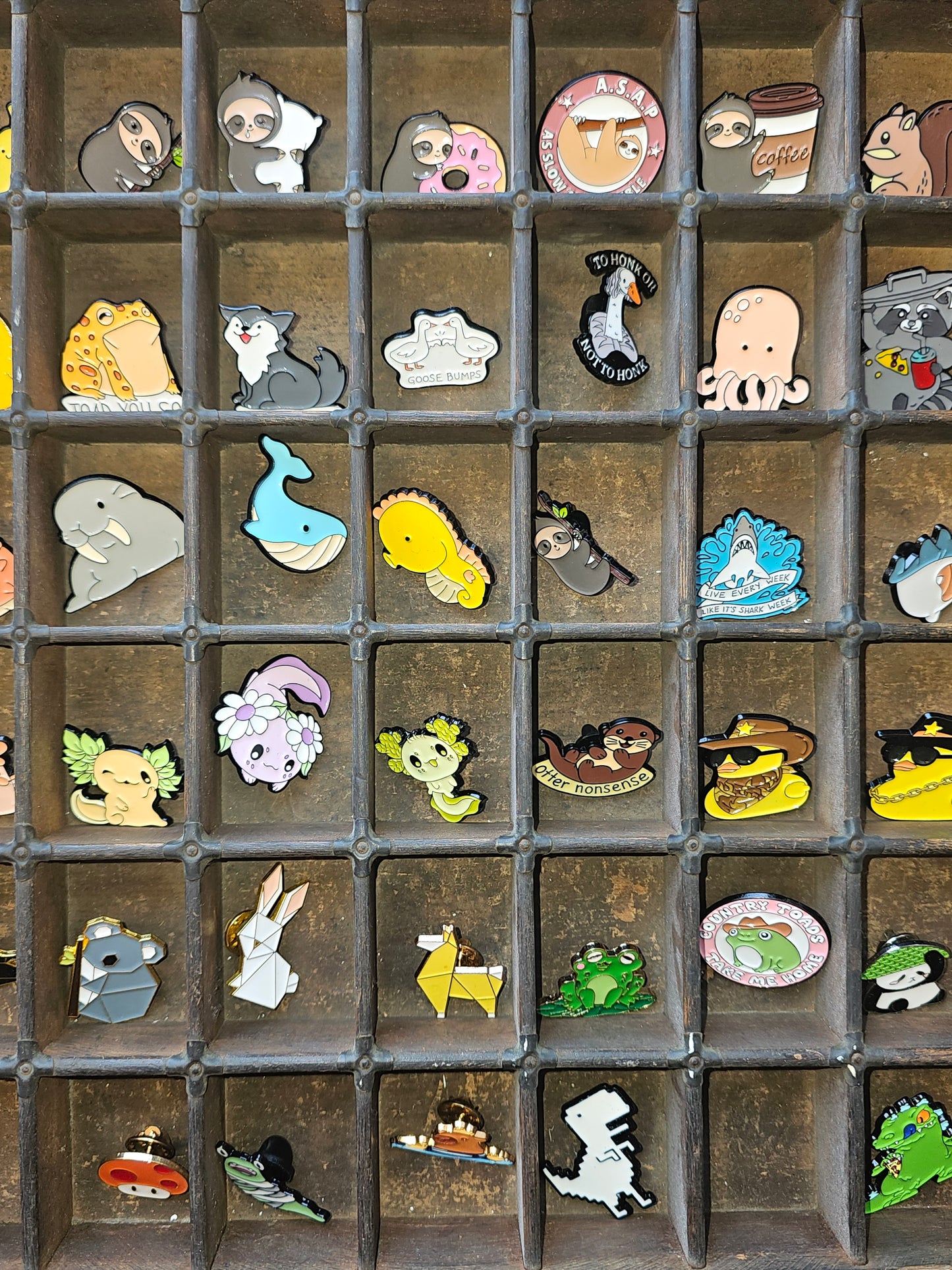 Collection of colorful pin badges displayed in a wooden tray, showcasing various cute designs.
