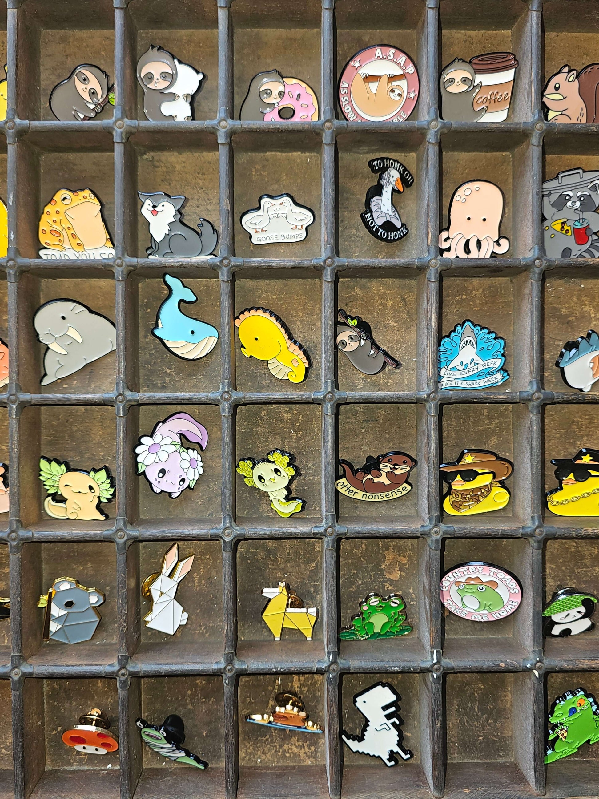 Collection of colorful pin badges displayed in a wooden tray, showcasing various cute designs.