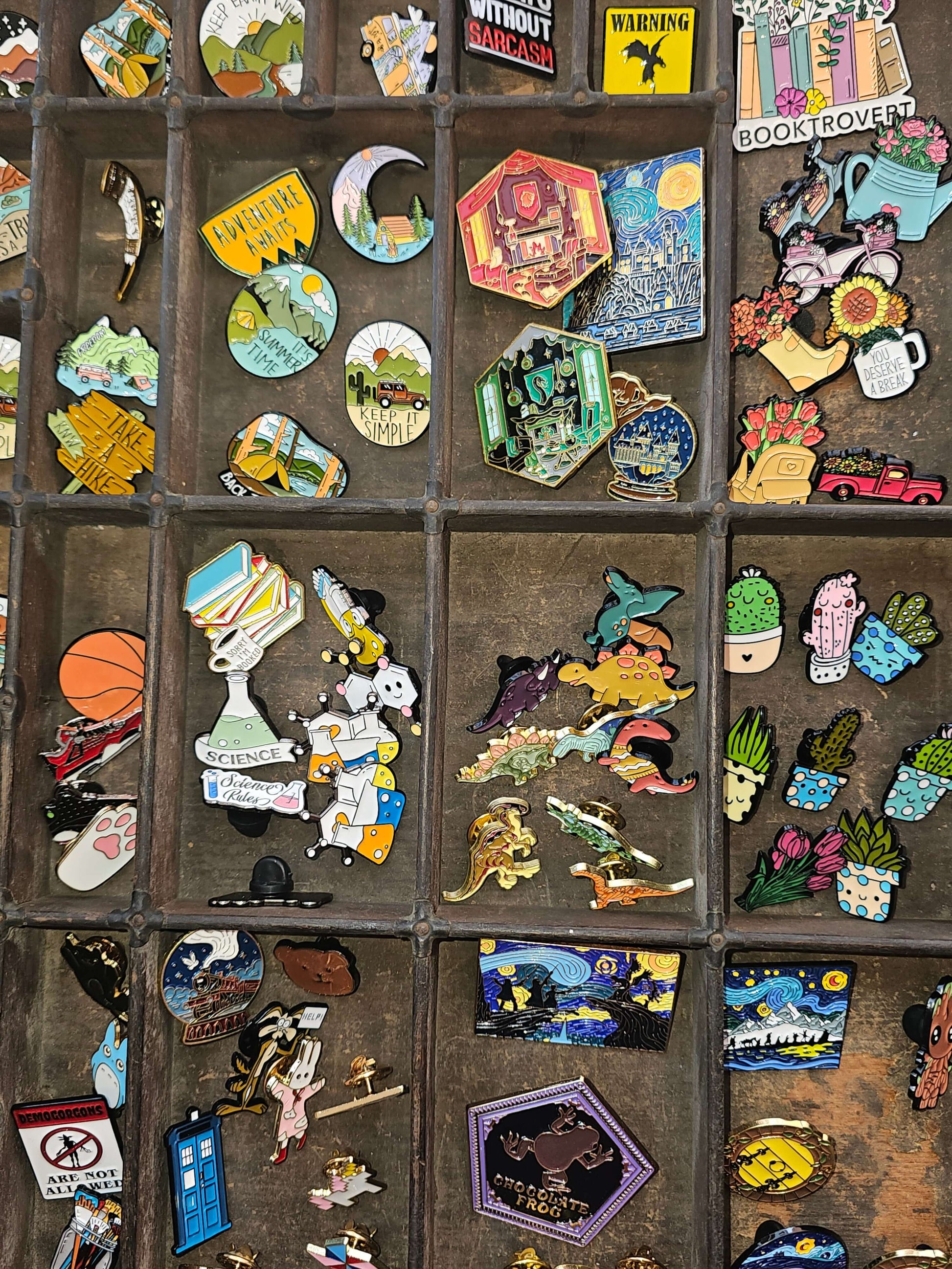 Colorful assortment of enamel pin badges displayed in a vintage organizer, showcasing various fun designs.
