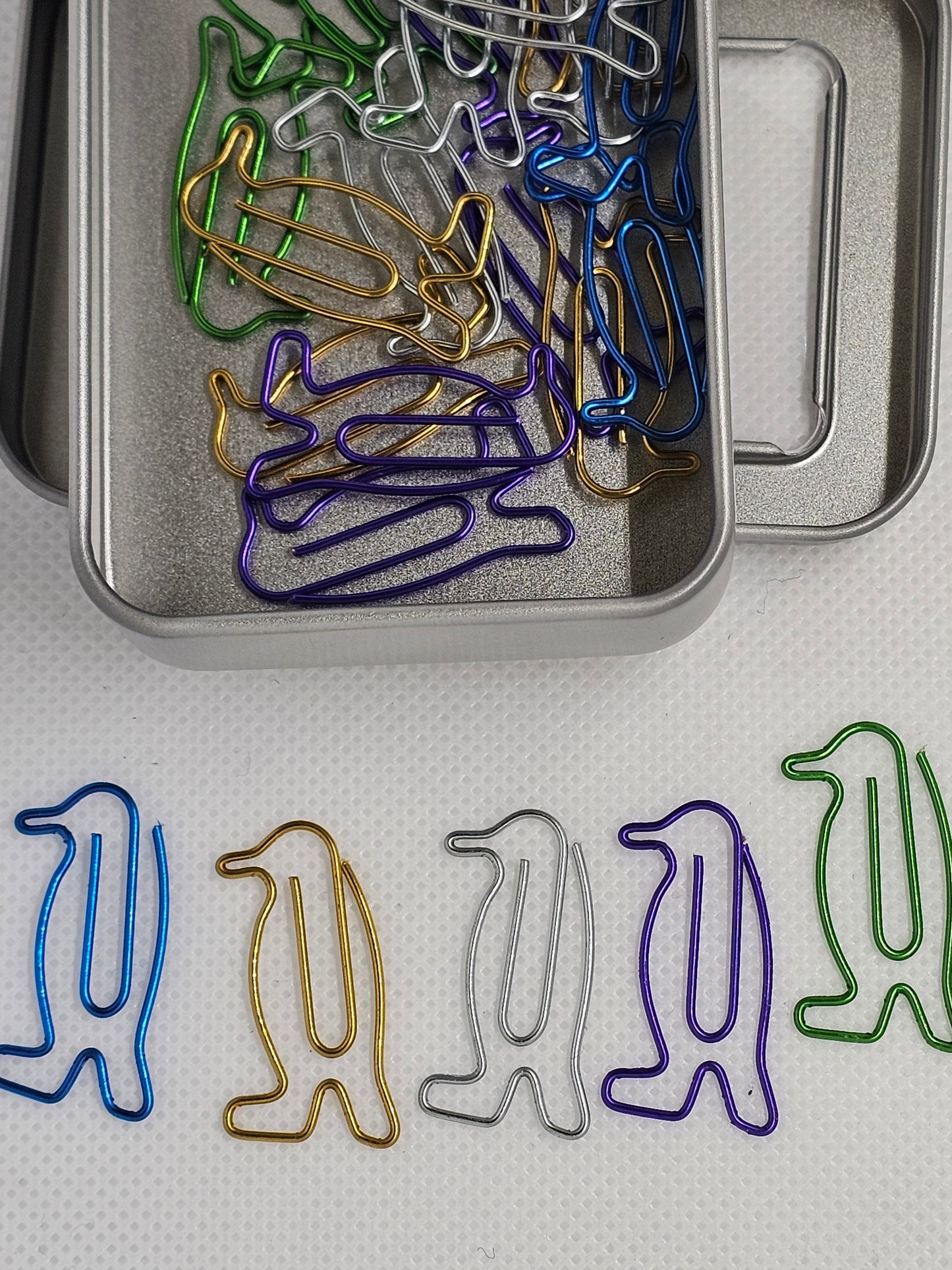 Colorful animal-shaped paper clips in a tin on a textured surface