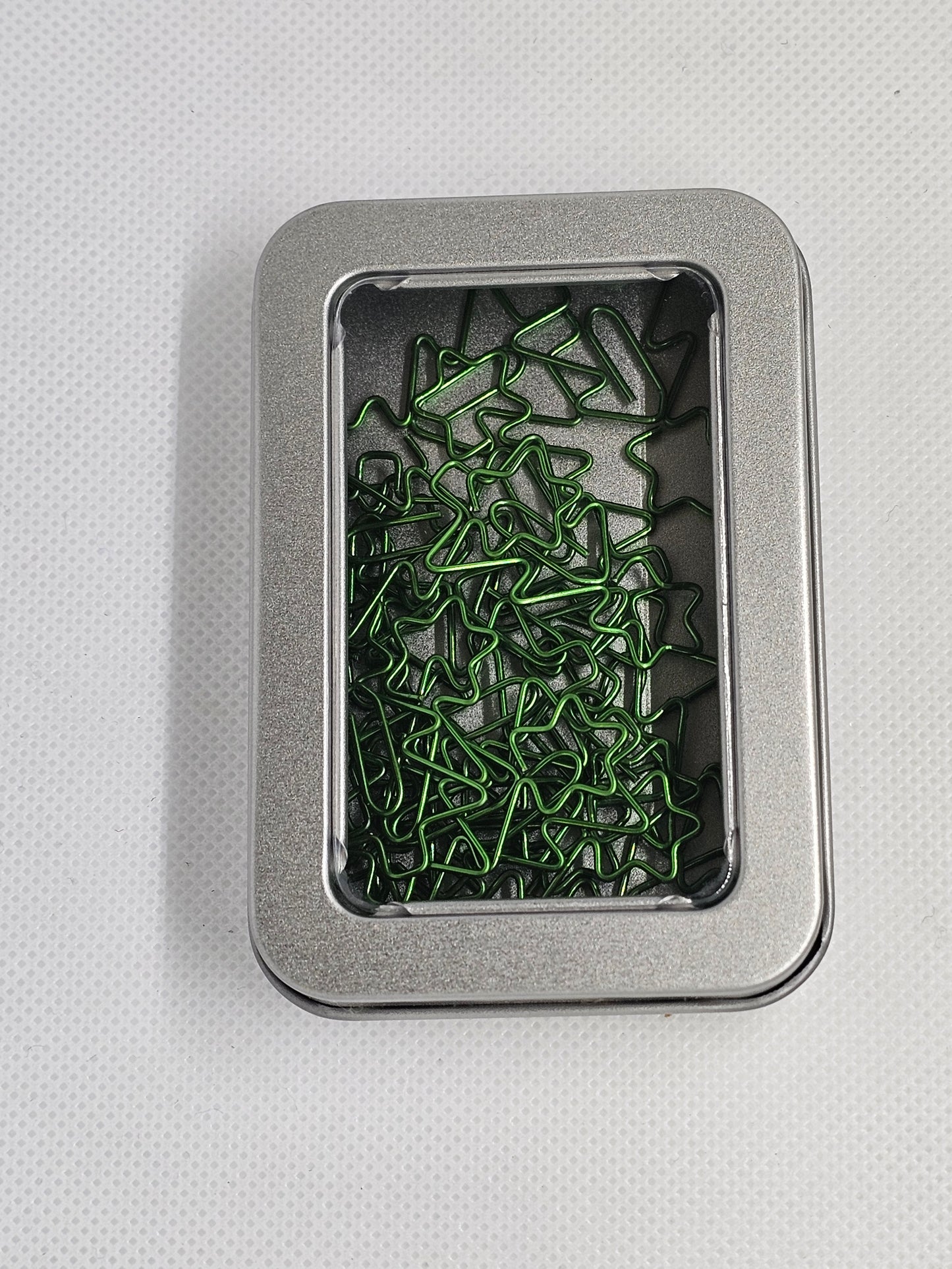 Metal tin with green paper clips on a light gray background