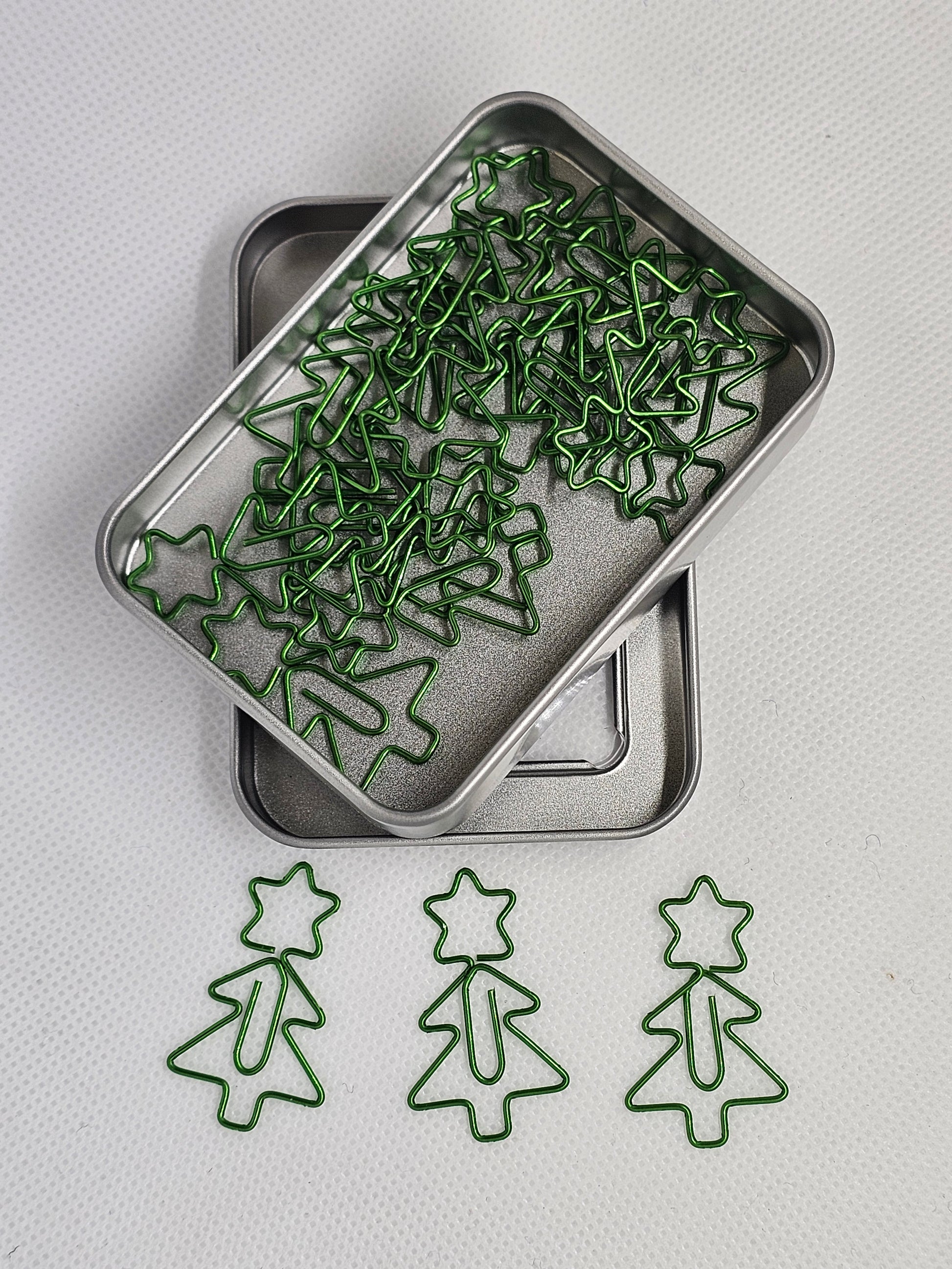 Green paper clips shaped like Christmas trees on a metal tray with more paper clips on a white background.