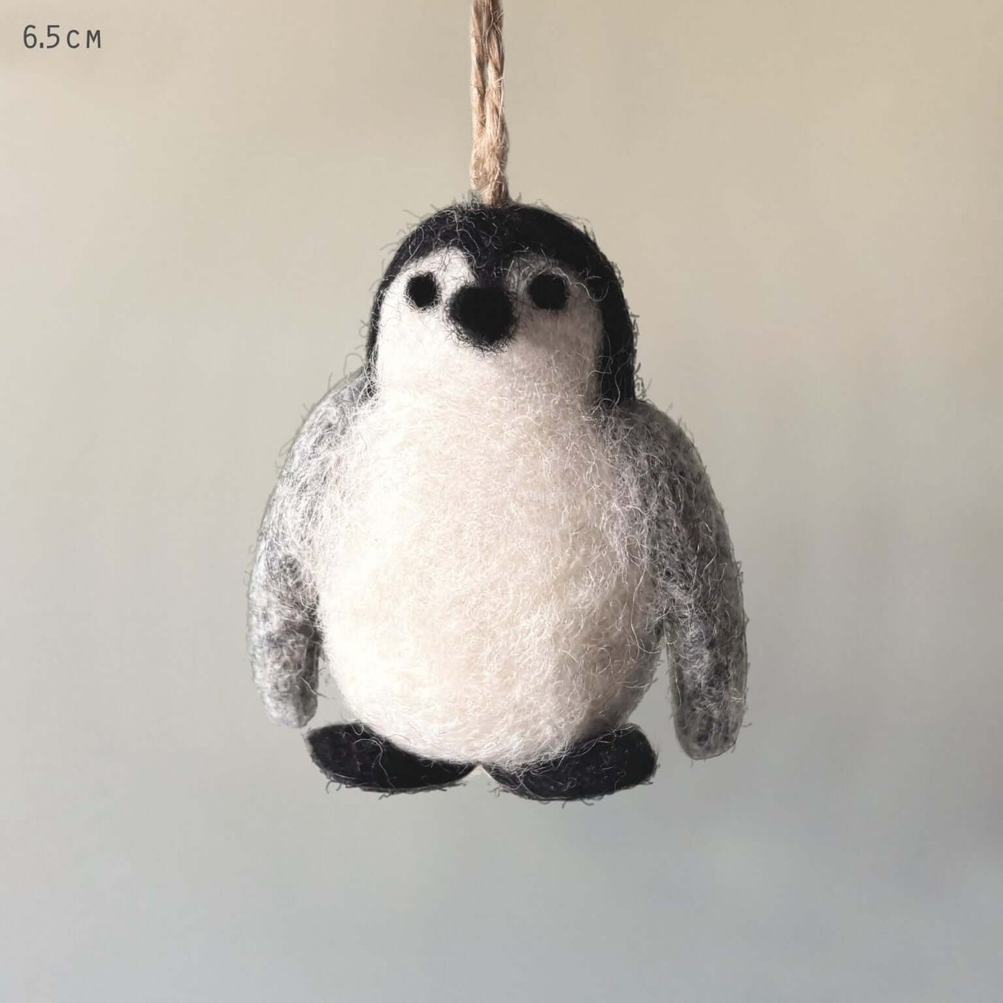 Felted penguin ornament hanging on a string against a neutral background