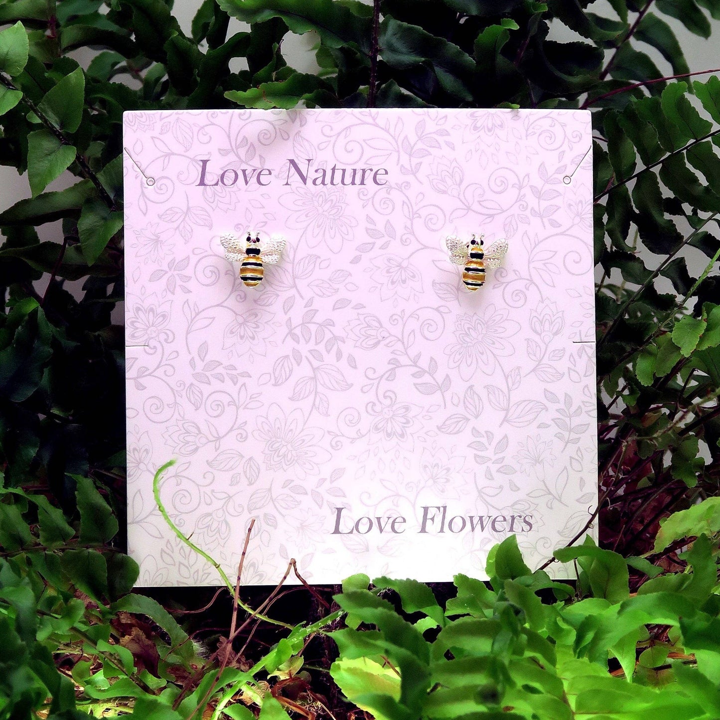Bee-shaped earrings on a 'Love Nature, Love Flowers' card with green foliage in the background