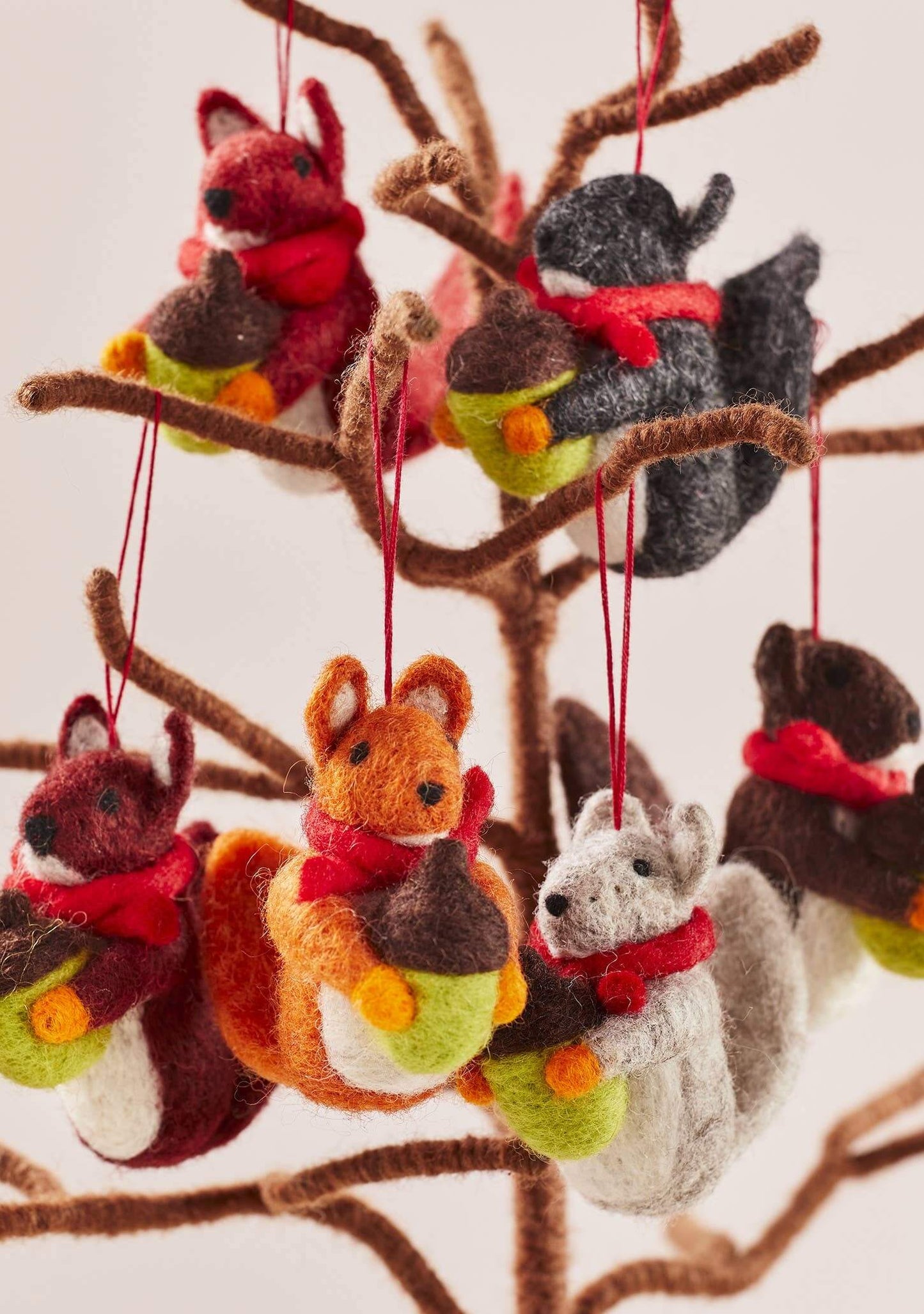 Felted animal ornaments including a fox, deer, and squirrel hanging from a branch.