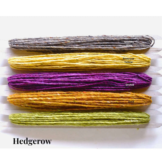 Five colors of Donegal weaving yarn: Smokey Gray, Primrose Yellow, Orchid, Gold, and Pear Green on card shuttles.