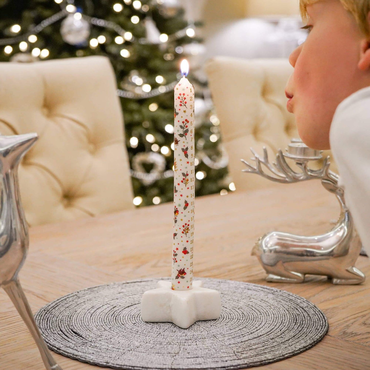 Decorative candle with floral design on a stand in front of a Christmas tree.