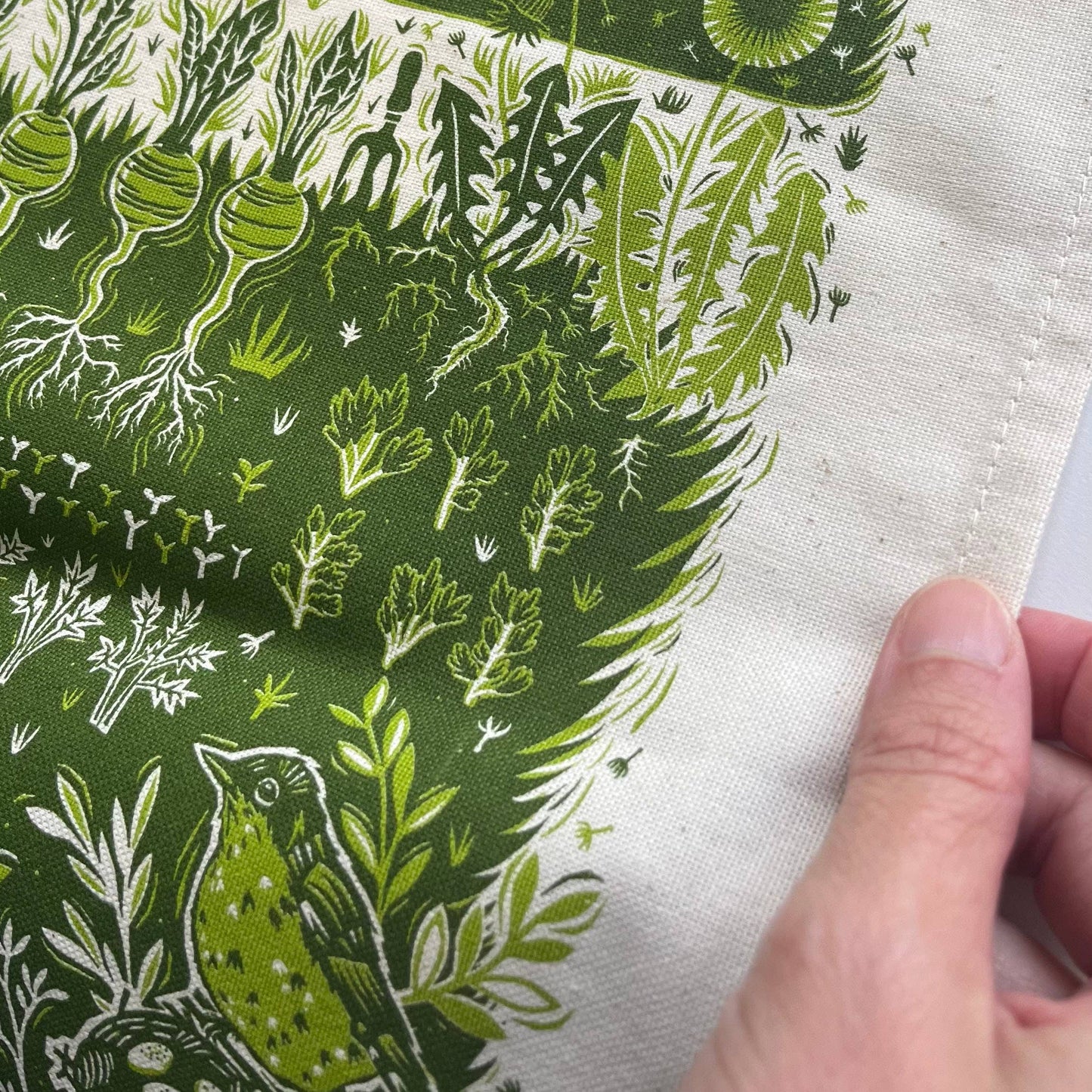 Close-up of a hand holding fabric with green and white botanical pattern