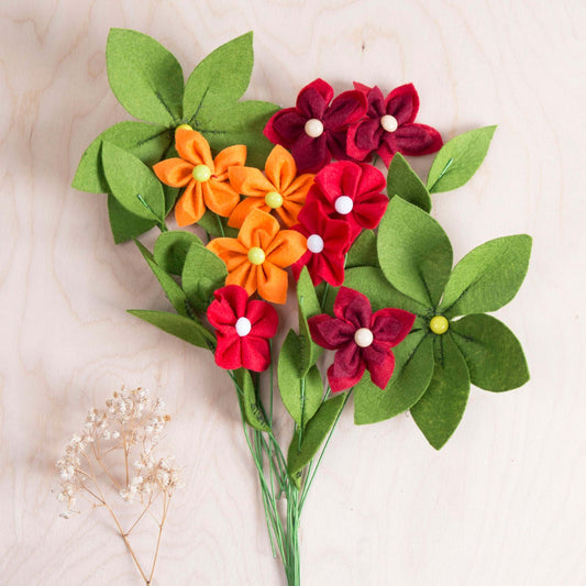 Colorful felt flower bouquet with green leaves, showcasing vibrant reds, yellows, and oranges, perfect for home decor.