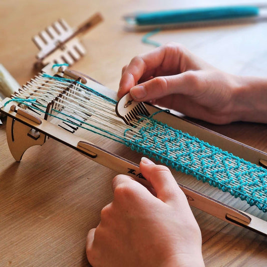 Person weaving with a wooden Rocket Loom using vibrant yarn in a bracelet kit from Pop Out Projects.