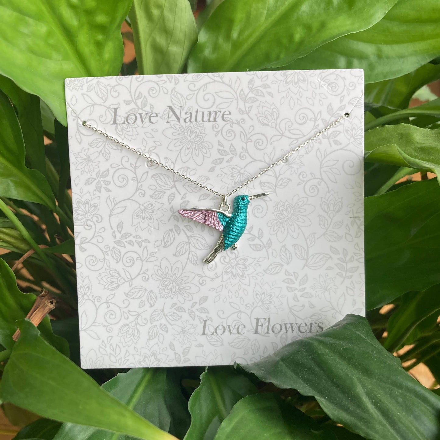 Hummingbird necklace on a 'Love Nature Love Flowers' card with green leaves in the background