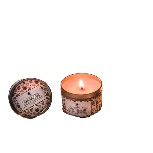 Hot chocolate candle, glass mug with hot chocolate, and book on a soft surface with string lights.