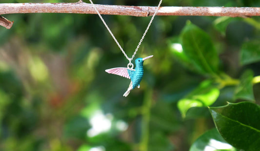 Turquoise hummingbird necklace on a chain against a blurred green leafy background