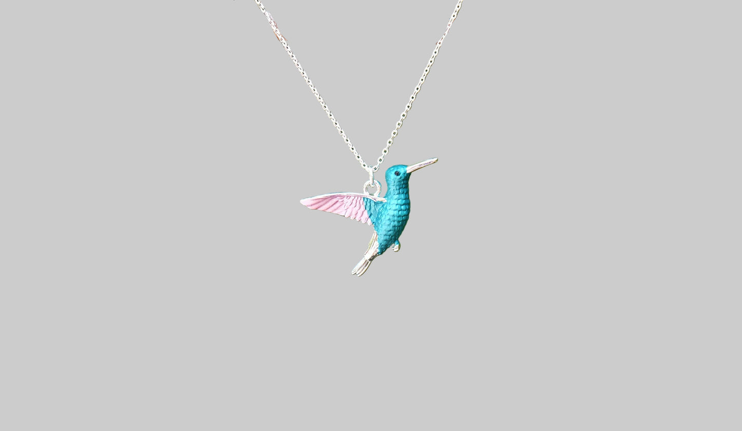 Teal hummingbird pendant on a silver chain against a light gray background