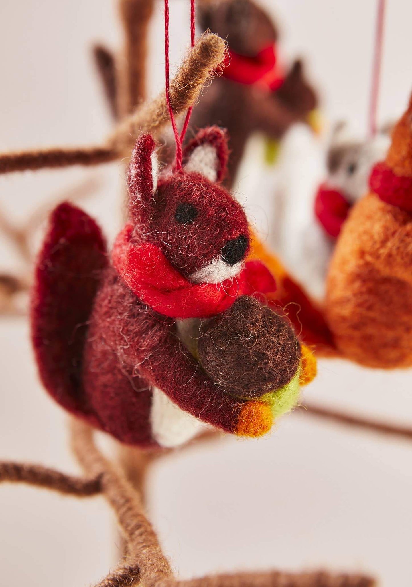 Felted squirrel ornament with a red scarf hanging on a branch.