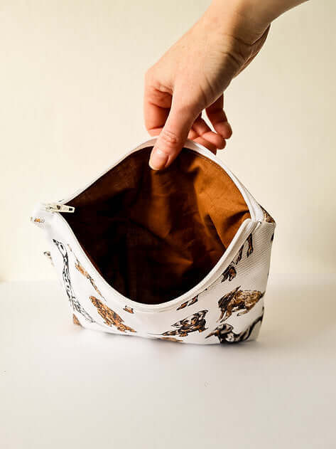 Hand holding a small, patterned pouch with a reflective interior on a neutral background