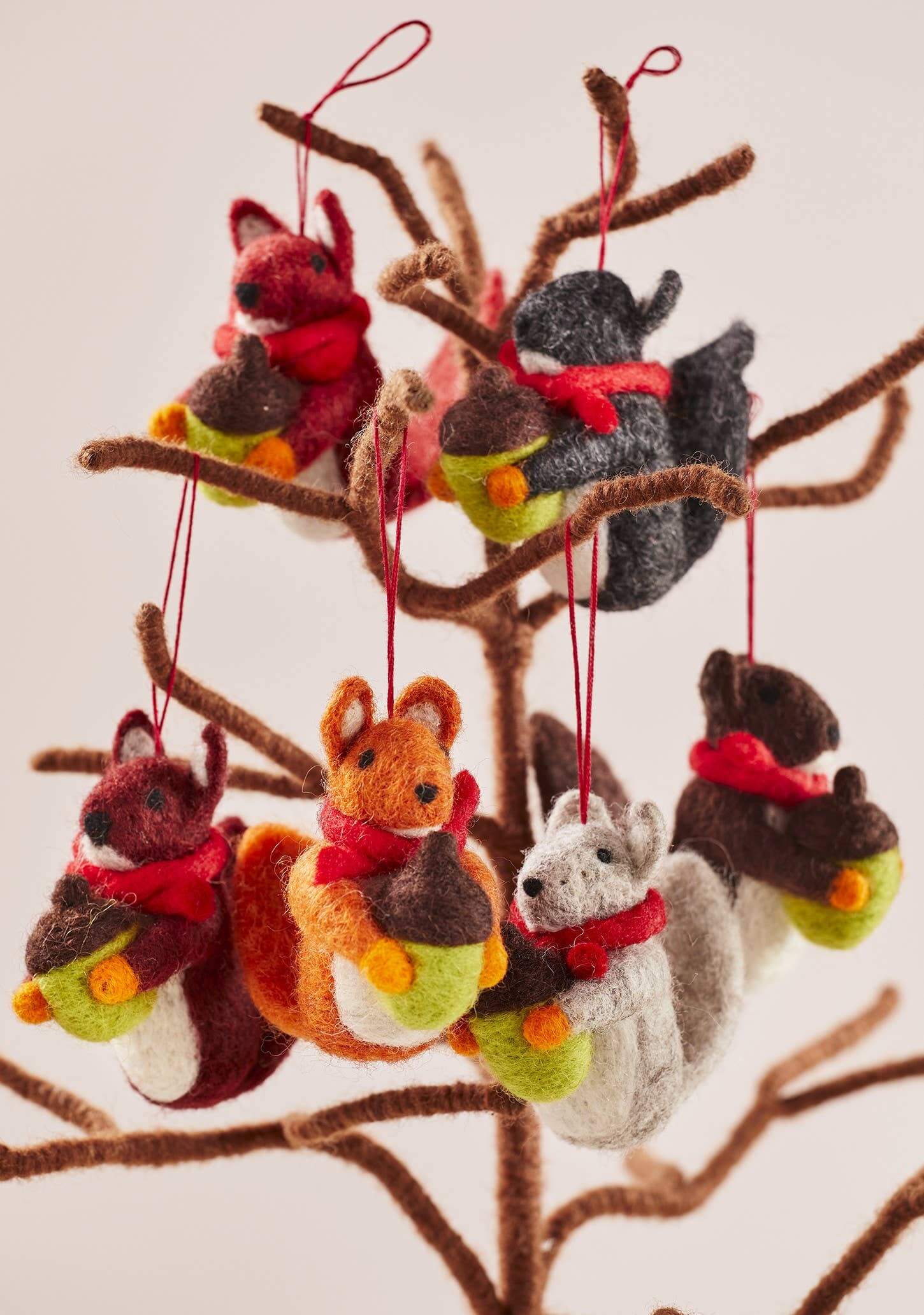 Felted animal ornaments including fox, squirrel, and raccoon hanging from a branch.