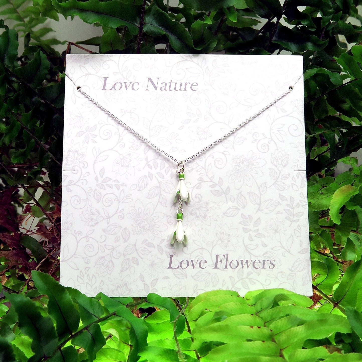 Necklace with pendant on a card with 'Love Nature' and 'Love Flowers' text, surrounded by green foliage.