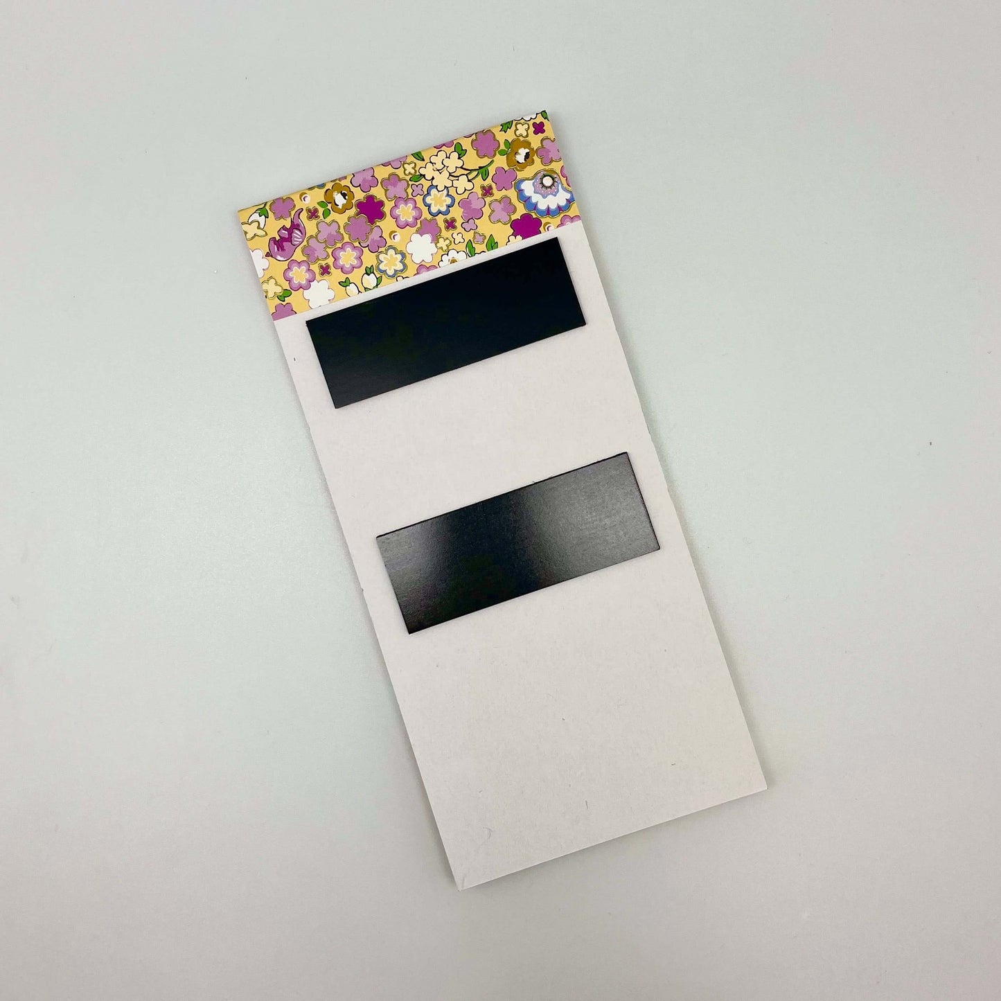 Floral-patterned notepad with black magnetic strips on a light gray background