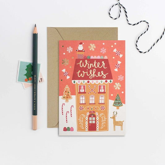 Christmas card with gingerbread house design and 'Winter Wishes' text, accompanied by a pencil and decorative string.