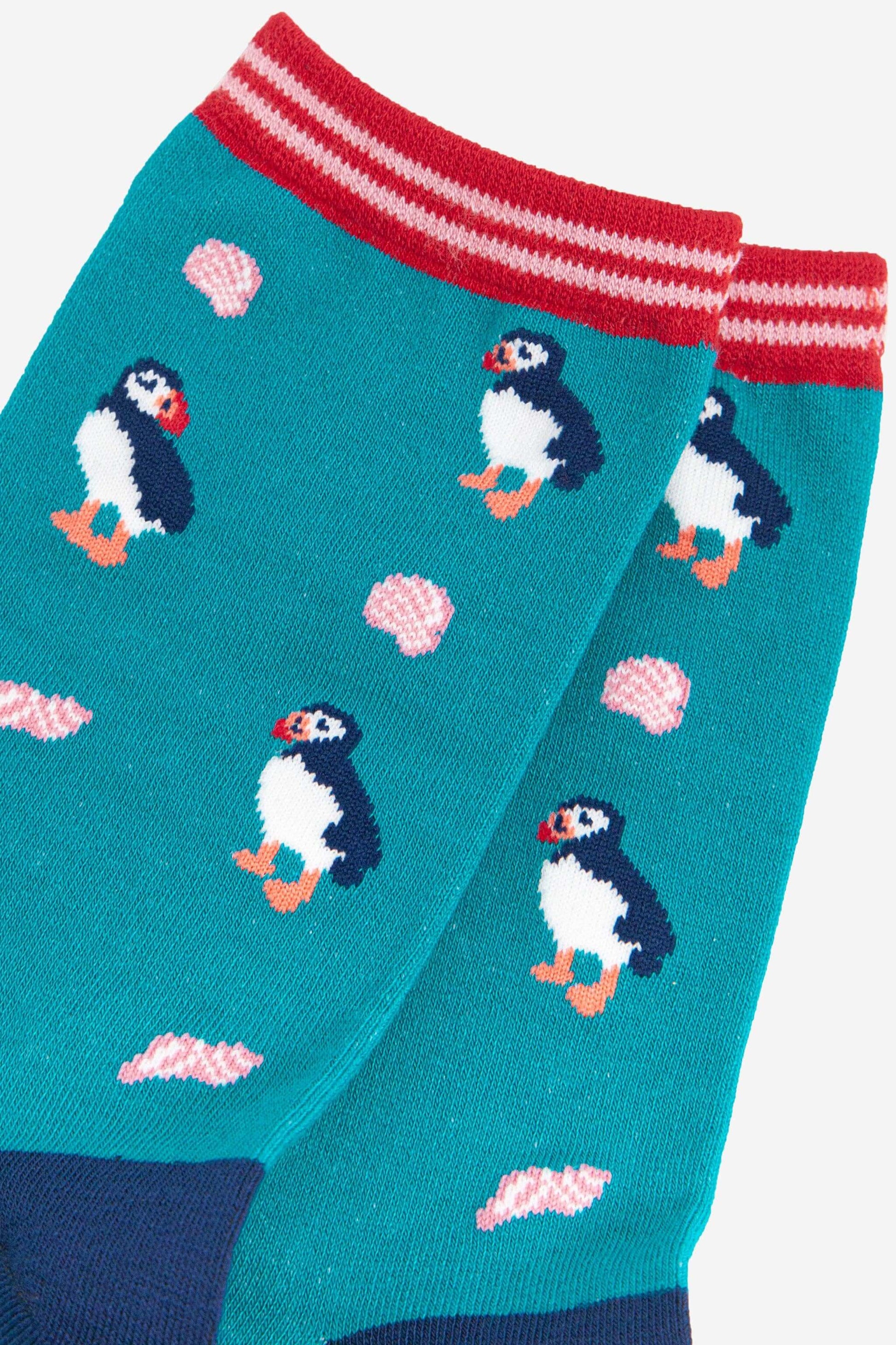 Teal sock with puffin pattern and red and white striped top on a light blue background