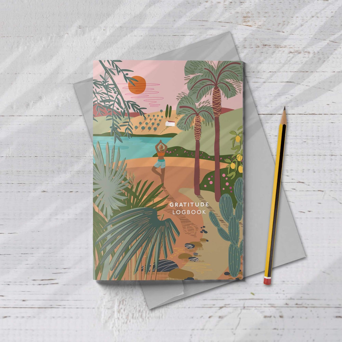 A5 Gratitude Logbook with yoga cover illustration, surrounded by a gray envelope and pencil, evoking calm and nature.
