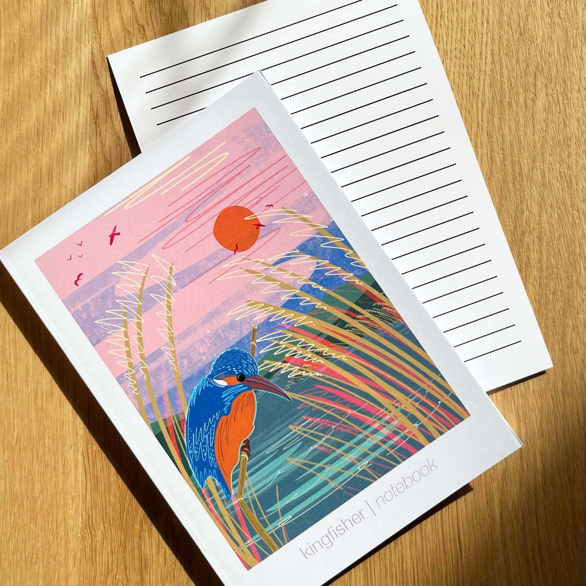Kingfisher notebook featuring vibrant illustration, blank interior with lined sheet insert, placed on a wooden surface.