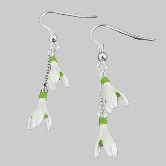 Silver earrings with white floral charms on a gray stone background