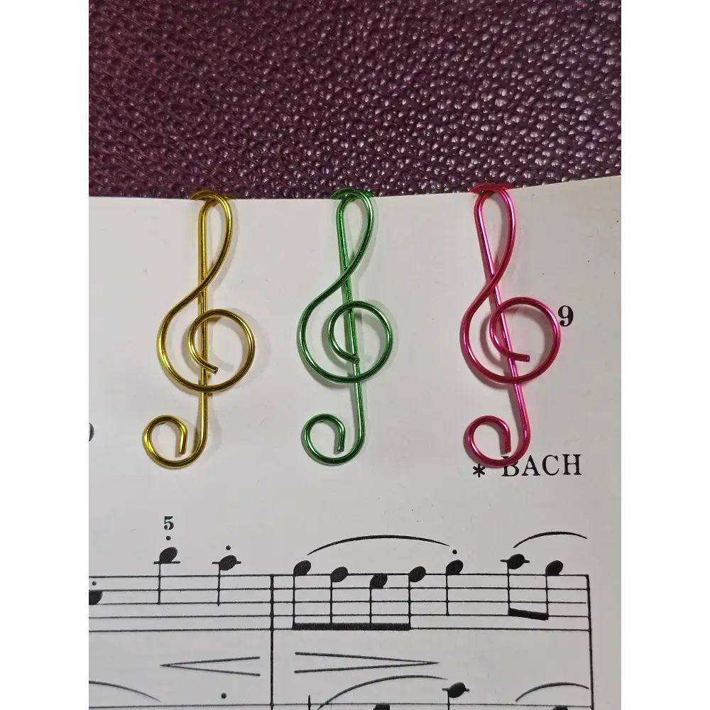 Three colorful musical note paper clips in gold, green, and pink holding sheet music with Bach's composition.