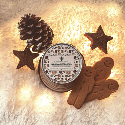 Candle labeled 'Baked Gingerbread' surrounded by decorative gingerbread men, stars, and a pine cone on a soft surface.