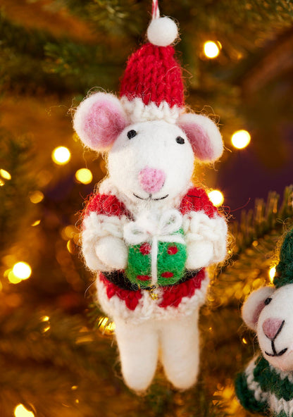 Knitted mouse ornament in a red hat and sweater holding a green gift box, Christmas tree background.