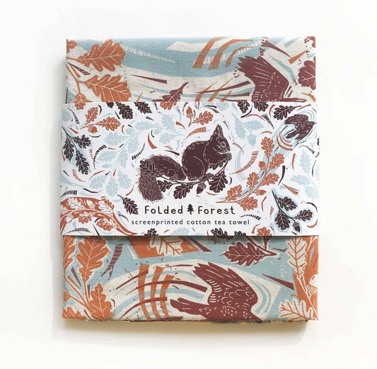 Packaged cotton tea towels with forest-themed design on a white background
