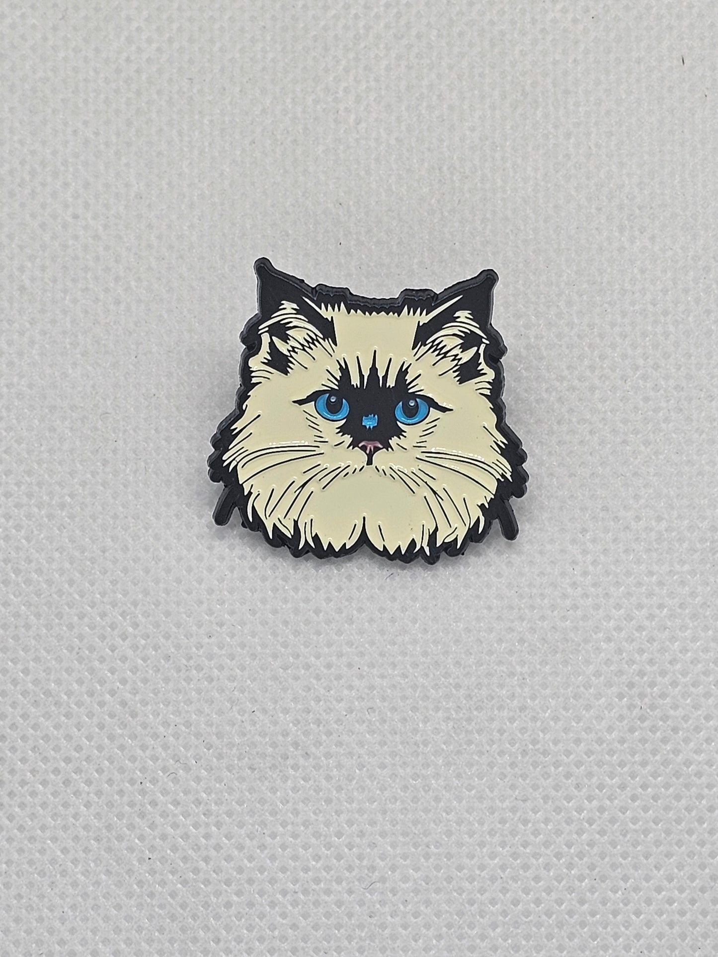 Enamel pin badge featuring a fluffy cat design with blue eyes, perfect for pet lovers.