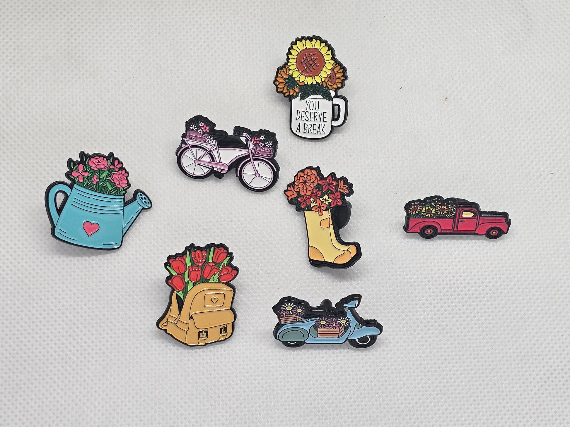 Colorful plant themed enamel pin badges featuring flowers in various designs like watering can, bicycle, and truck.