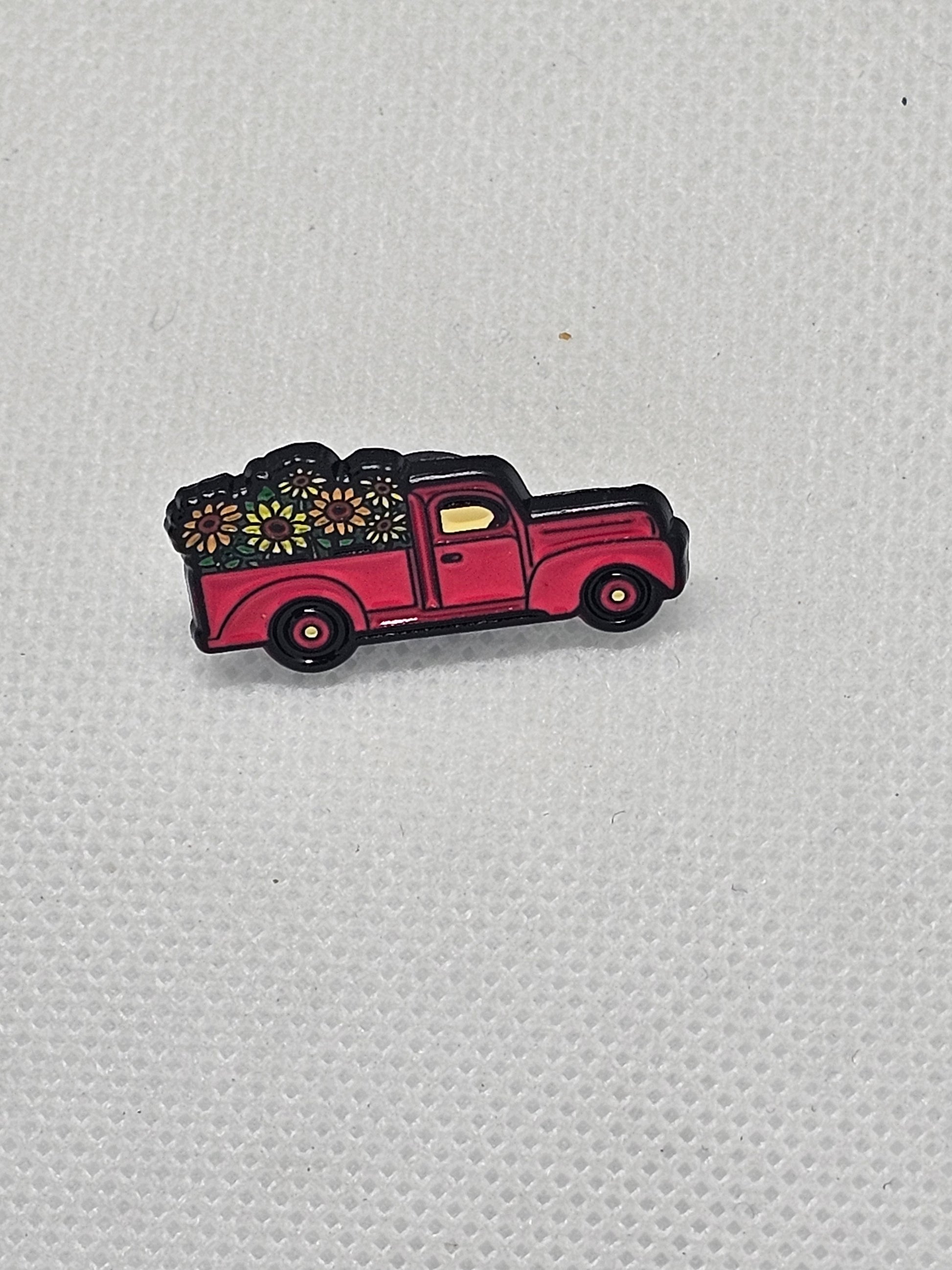 Red enamel pin badge of a vintage truck carrying colorful flowers, perfect for plant lovers.