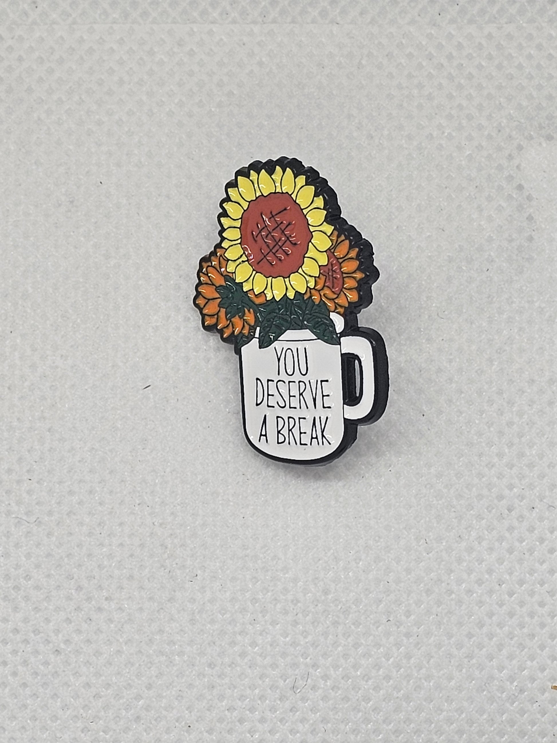 Colorful enamel pin badge featuring sunflowers and text "You Deserve a Break" for plant lovers.