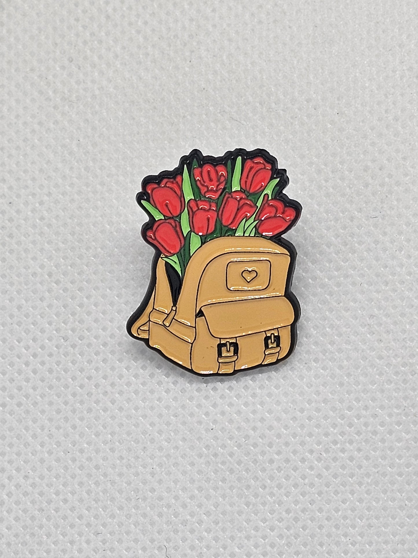 Enamel pin badge featuring a cute backpack with red tulips for plant lovers. Perfect accessory for any nature enthusiast.