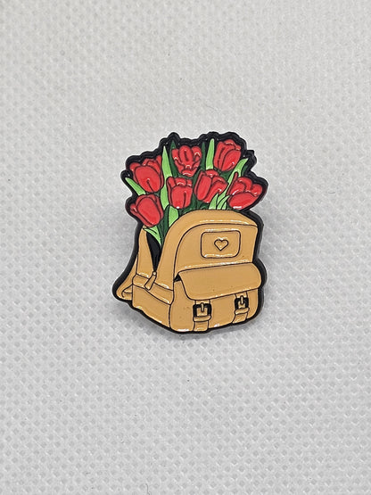Enamel pin badge featuring a cute backpack with red tulips for plant lovers. Perfect accessory for any nature enthusiast.
