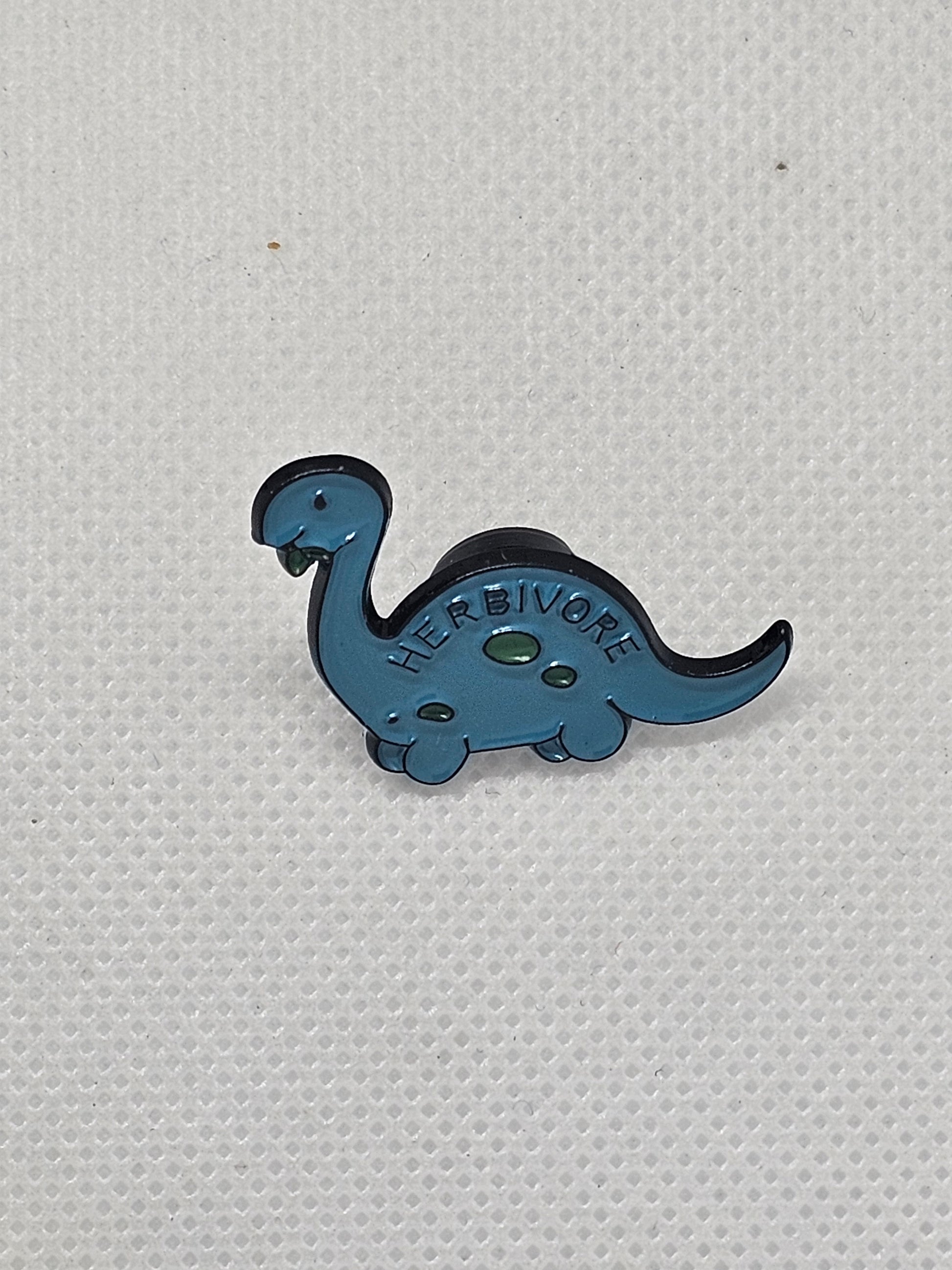 Cute blue herbivore dinosaur pin badge, perfect accessory for bags or clothing, ideal for dinosaur lovers.