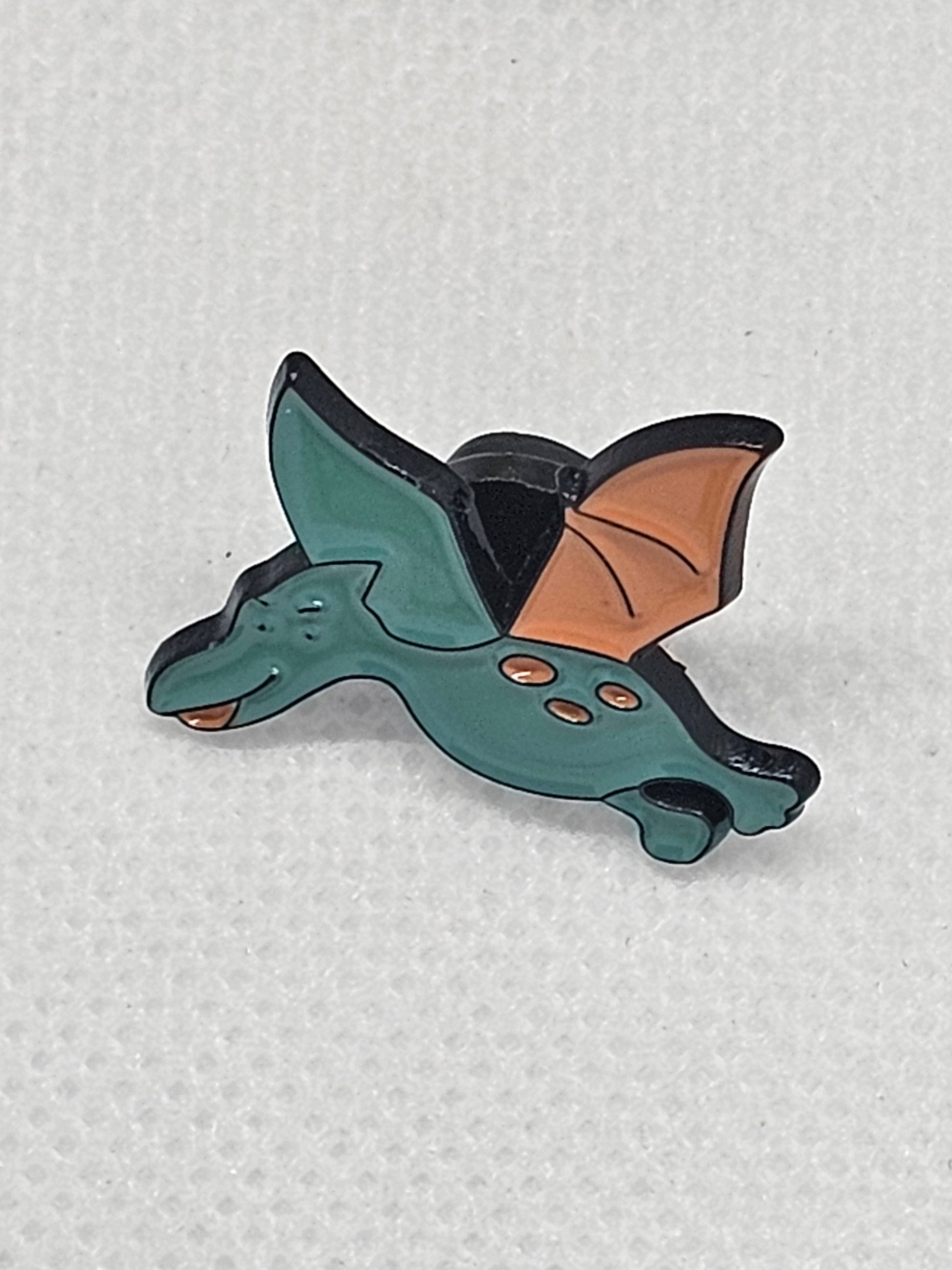 Flying dinosaur enamel pin badge with green and orange design, perfect for dinosaur lovers and as a bag accessory.