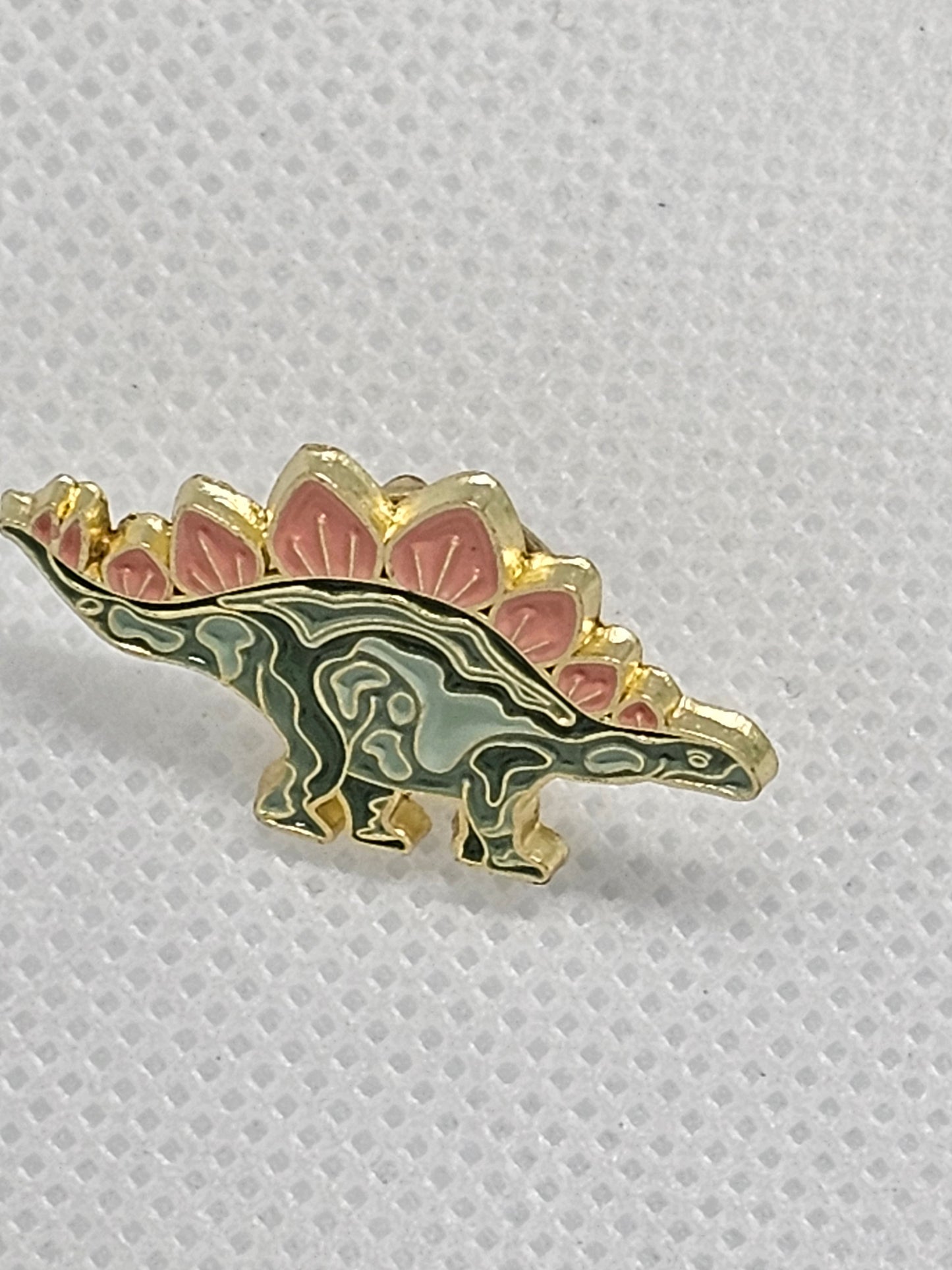 Cute enamel stegosaurus pin badge, perfect for dinosaur lovers. Ideal accessory for bags or clothing.