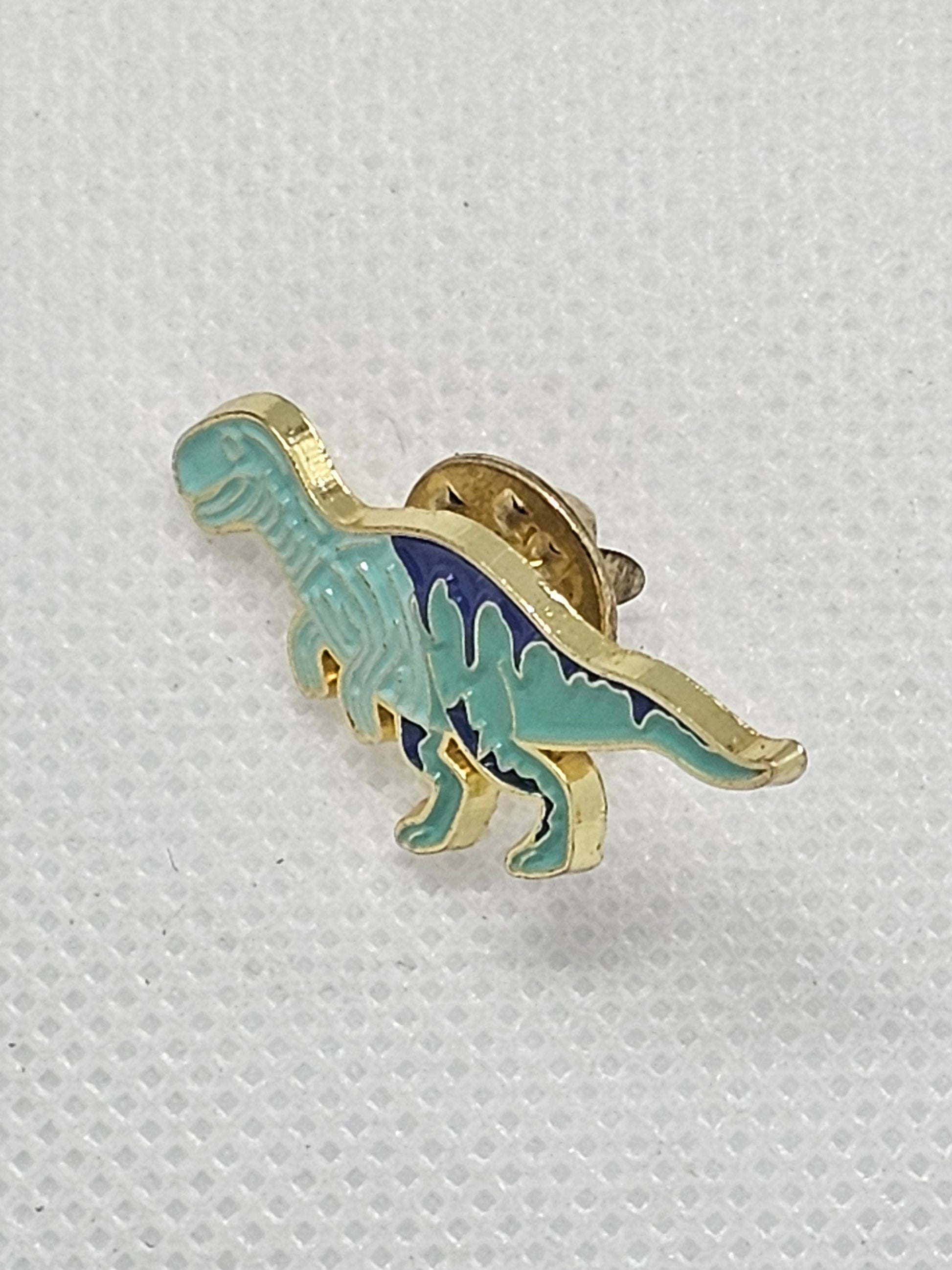 Cute dinosaur enamel pin badge in turquoise and gold, perfect for accessories and dinosaur lovers.