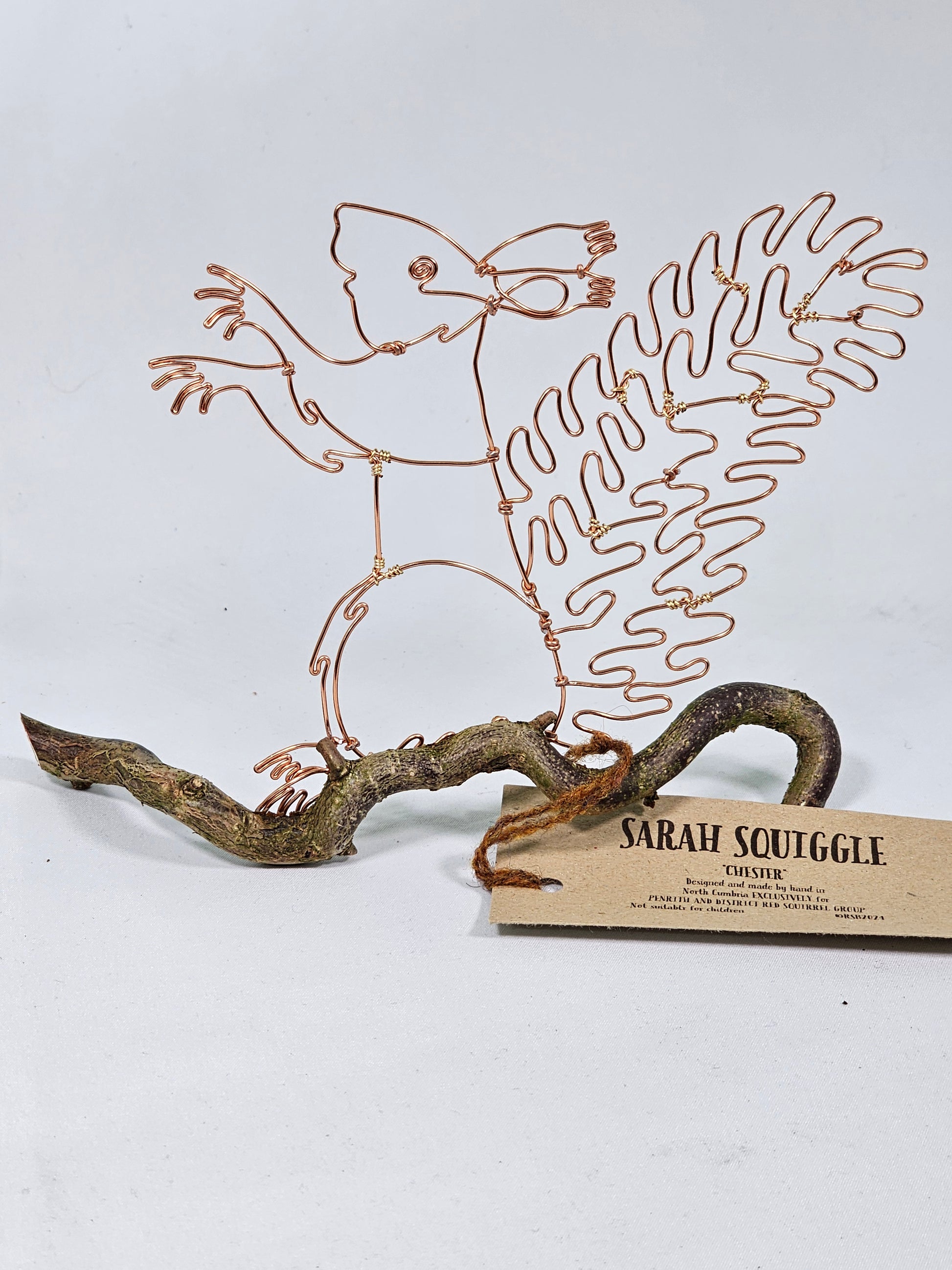 Decorative metal wall art of a Squirrel on a branch with a cardboard tag.