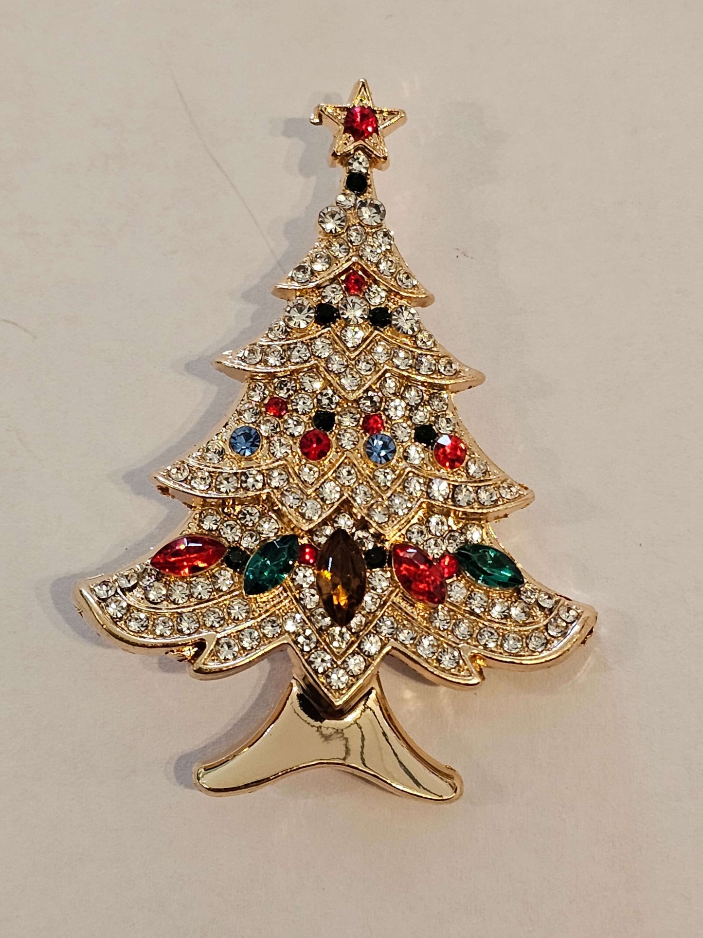 Decorative Christmas Tree shaped brooch with gemstones on a beige background