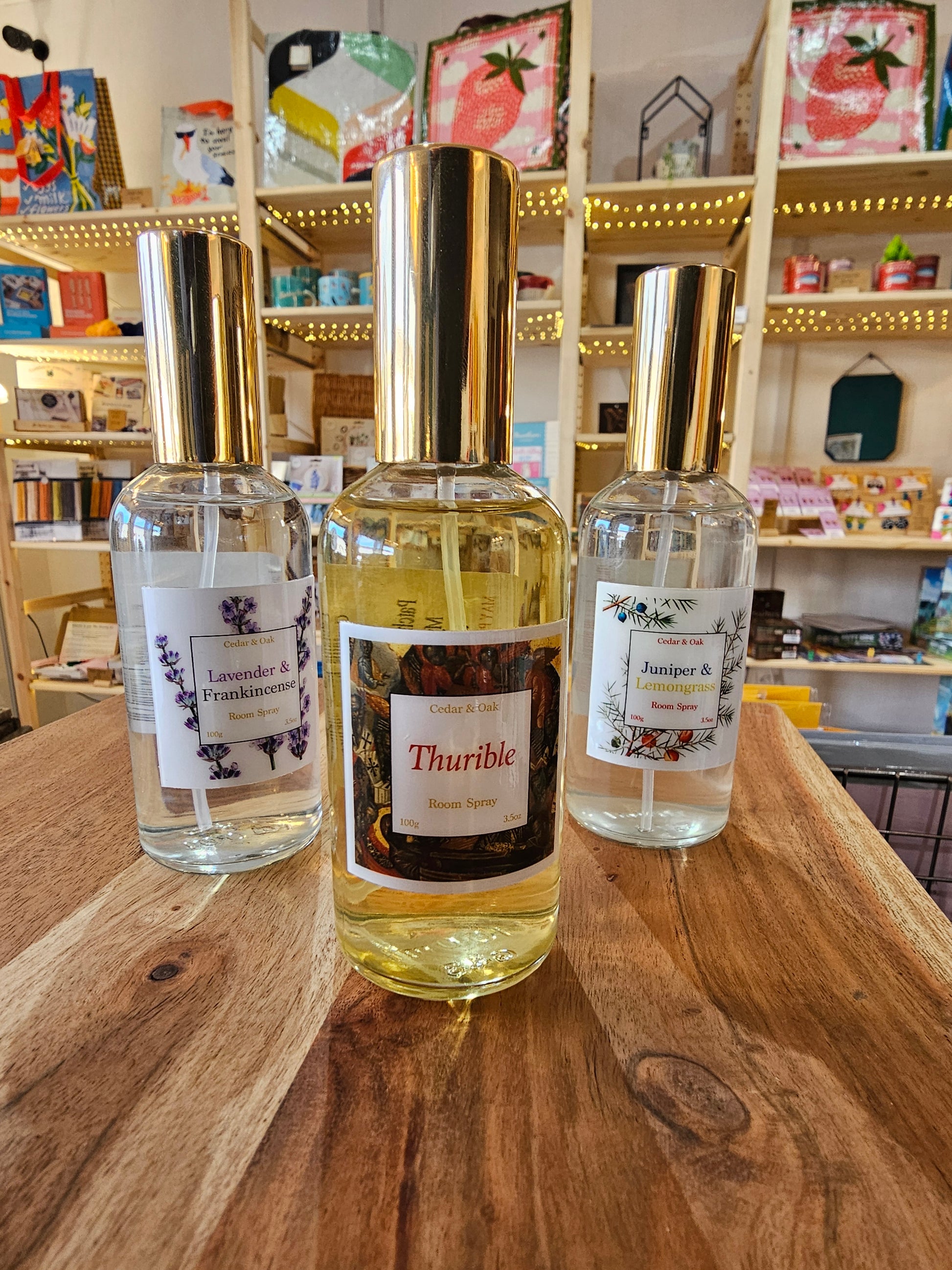 Three bottles of room spray on a wooden surface with a blurred store interior in the background.